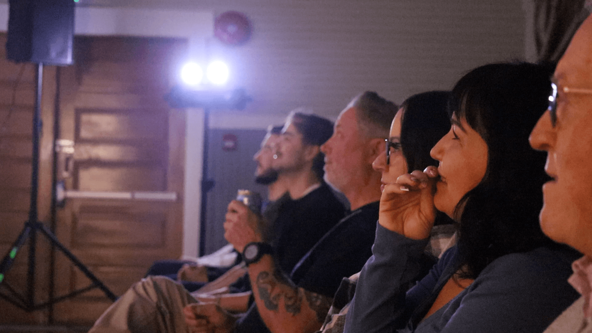 The front row laughing under the stage lights, one person with a hand over their mouth.